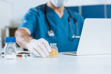 Lateks eldivenli doktorun laptopun yanında otururken kapsüllü cam kabı alıp...