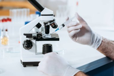 Lateks eldivenli biyolog mikroskobun yanında şırınga tutuyor.