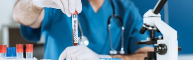 Lateks eldivenli bilim adamlarının Coronavirus yazıtlı test tüpü tutarken çekilmiş görüntüsü, panoramik çekim