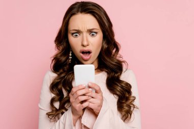 shocked girl looking at smartphone isolated on pink  clipart