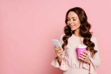 Mutlu kız akıllı telefon kullanıyor ve pembe bardakta kağıt bardak tutuyor. 