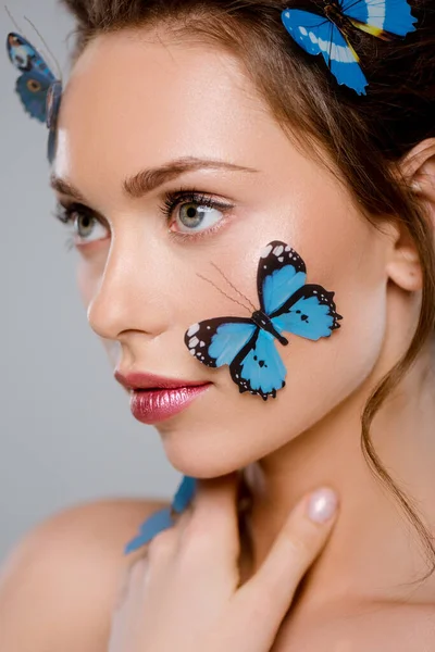 selective focus of young woman with blue decorative butterflies on face isolated on grey
