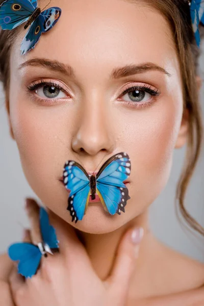 close up attractive young woman with decorative butterflies on face isolated on grey