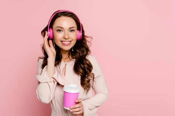 快乐的女孩在无线耳机里听着音乐 手里拿着用粉色隔开的纸杯 — 图库照片