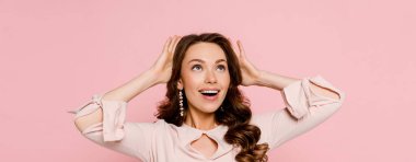 Pembe üzerinde izole edilmiş kıvırcık saçlara dokunan heyecanlı genç kadının panoramik görüntüsü. 