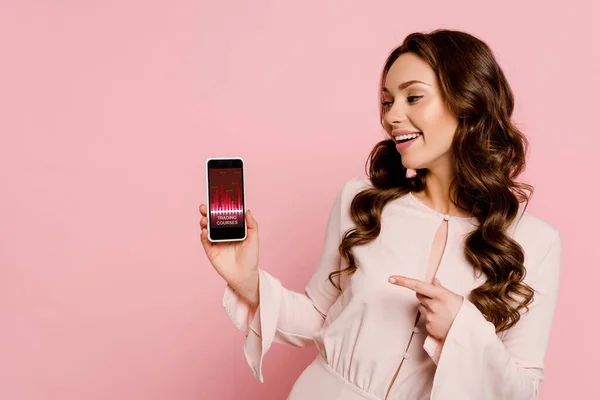 Wesoła Dziewczyna Wskazując Palcem Smartfona Kursów Handlowych Ekranie Odizolowany Różowy — Zdjęcie stockowe