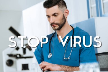 Mikroskop yakınındaki dizüstü bilgisayarda yazan konsantre doktorun seçici odağı, virüs illüstrasyonunu durdur