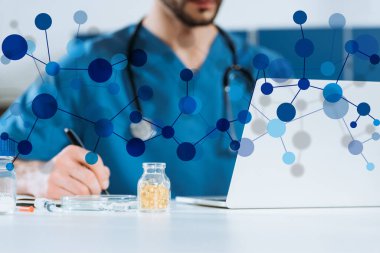 Laptop 'ın yanında yazan genç doktorun seçici odak noktası ve ilaç içeren kap, molekül yapısı çizimi