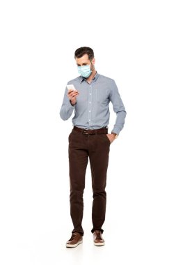 Tıbbi maskeli bir işadamı el ele durur ve beyaz üzerine izole edilmiş akıllı telefon kullanır. 