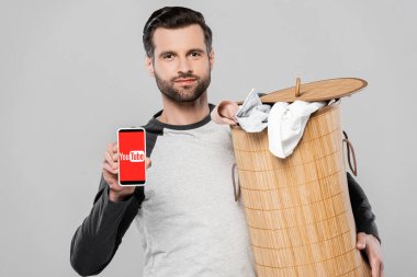 KYIV, UKRAINE - 23 Mart 2020: Gri ekranda youtube uygulaması ile çamaşır sepeti ve akıllı telefon tutan yakışıklı adam