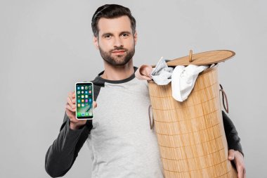 KYIV, UKRAINE - 23 Mart 2020: Çamaşır sepeti tutan yakışıklı adam ve iphone gri üzerinde izole edilmiş