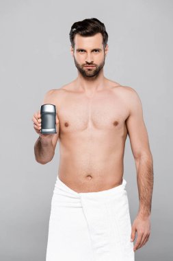 Havlu giymiş sakallı ve kaslı adam gri renkte deodorant tutuyor. 