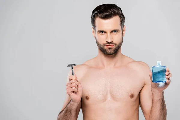 胡子和肌肉的男人在剃须后拿着乳液和剃须刀 用灰色隔离 — 图库照片