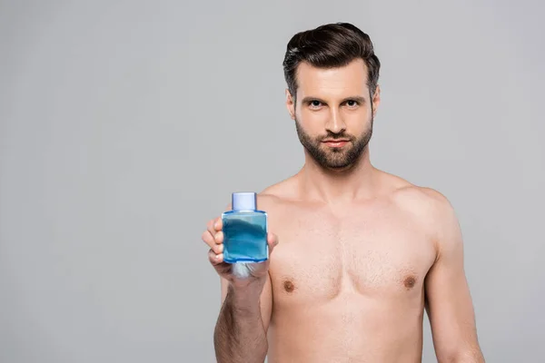 灰色で単離された剃り化粧水の後に青で瓶を保持筋肉男 — ストック写真