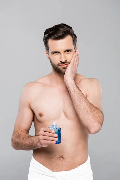 ローションを剃った後青い瓶を持ってる筋肉質の男灰色に隔離された触れる顔 — ストック写真