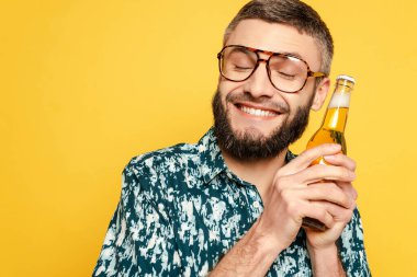 Gözlüklü, gülümseyen sakallı adam. Gözleri kapalı ve bira şişesi sarıya sarılı.