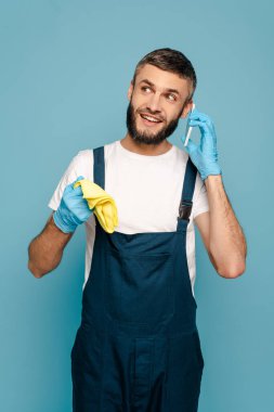 Üniformalı mutlu temizlikçi ve halılı lastik eldivenli akıllı telefondan konuşan mavi renkli.