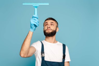 Mavi arka planda cam sileceği kullanarak üniformalı ve lastik eldivenli temizleyici