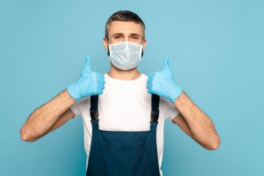 Tıbbi maskeli temizleyici mavi arkaplanda başparmak gösteriyor