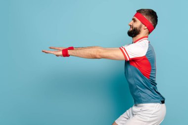 Mavi arka planda çömelmiş mutlu stil sporcusunun yan görünüşü