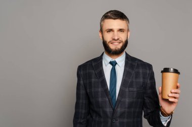 Gülümseyen, takım elbiseli, gri arka planda kahve içen yakışıklı iş adamı.