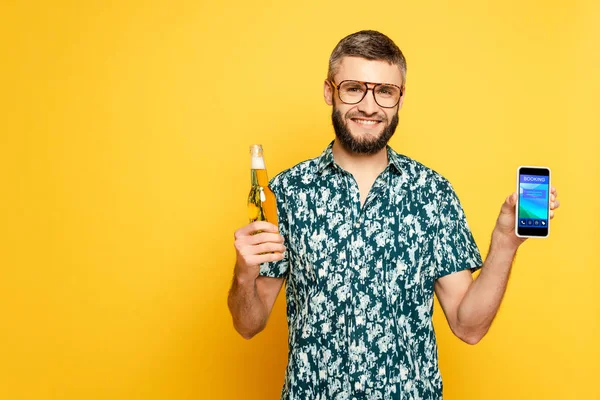 幸せな髭を生やした男でビールのさわやかなボトルを持っていますスマートフォンを示しています予約アプリで黄色 — ストック写真