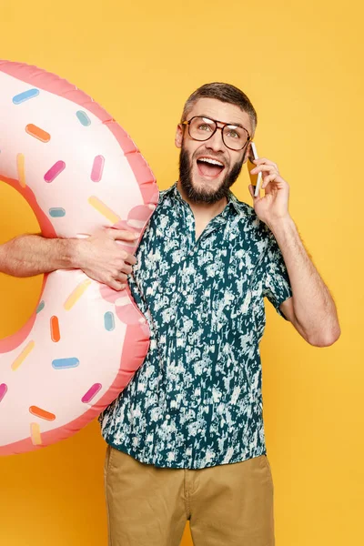 戴眼镜 留着胡子的快乐男人 带着甜甜圈 用智能手机用黄色说话 — 图库照片