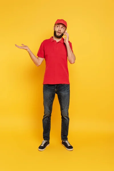 Förvirrad Skäggig Leverans Man Röd Uniform Talar Smartphone Gul — Stockfoto