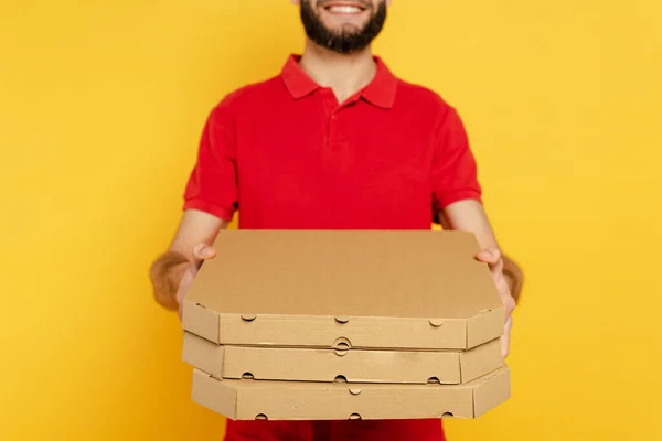 笑顔の髭を生やした配達人が赤い制服にピザボックスが黄色で隔離されてる — ストック写真