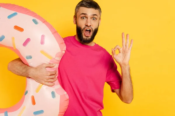 ショックを受けた髭男でピンクのTシャツで泳ぐリングショーOkサインは黄色に隔離された — ストック写真