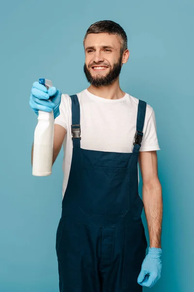 青い背景にスプレー洗剤を保持する均一なゴム手袋で幸せなクリーナー — ストック写真