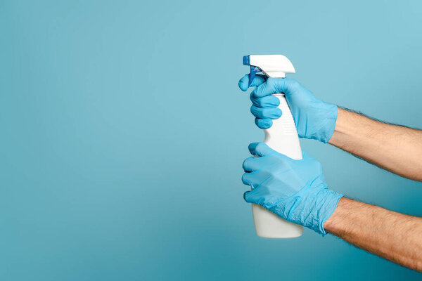 обрезанный вид чистящего средства в резиновых перчатках, держащих моющее средство на синем фоне

