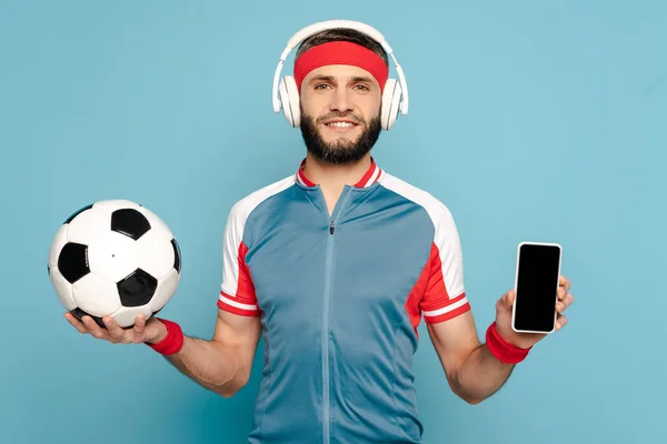 Vrolijke Stijlvolle Sportman Hoofdtelefoon Met Voetbal Smartphone Blauwe Achtergrond — Stockfoto