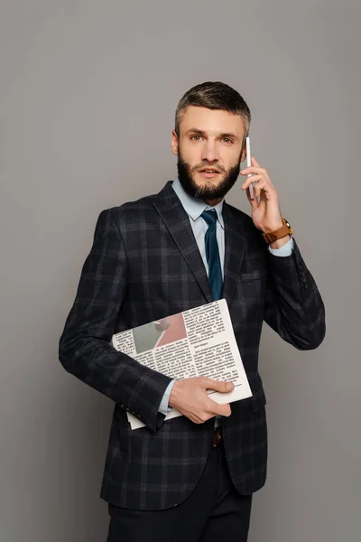 相貌俊俏 留着胡子的生意人 穿着西装 头戴灰色背景的报纸 用智能手机聊天 — 图库照片