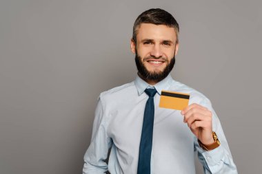 Gri arka planda kredi kartı olan yakışıklı, sakallı iş adamı.