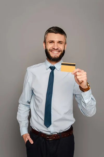 笑顔ハンサムな髭のビジネスマンクレジットカードでグレーの背景 — ストック写真