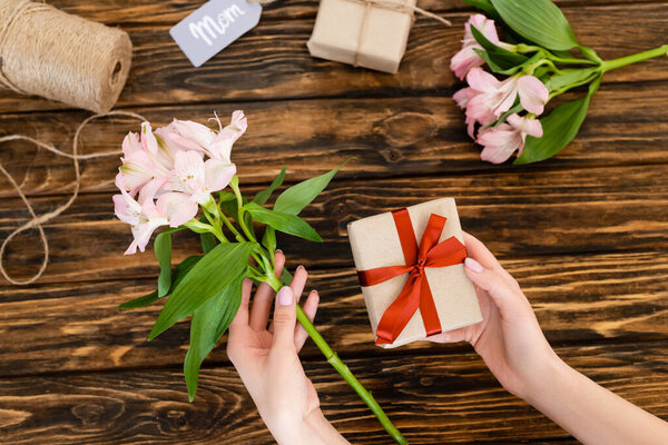 top view of woman holding pink flowers and present with red ribbon, mothers day concept 