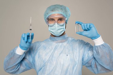 Koruyucu Google 'daki doktor ve tıbbi maske şırınga ve aşı kavanozunu gri renkte tutuyor.