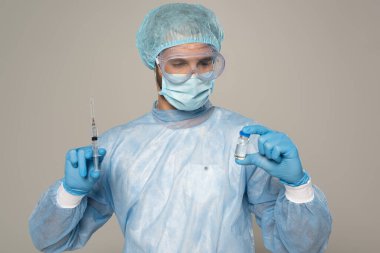 Tıbbi maskeli doktor ve koruyucu Google 'lar aşı ve şırınga kavanozunu gri renkte tutuyor.