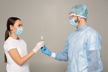 Doktorun tıbbi maske takan kadına el dezenfektanı verirken görüntüsü gri renkte.