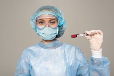 Tıbbi maskeli doktor ve koruyucu Google 'larda kan örneği ve koronavirüs içeren test tüpleri gri harflerle izole edilmiş.