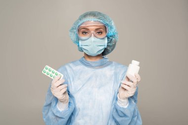 Tıbbi maskeli doktor ve koruyucu google 'lar gri renkte izole edilmiş su topladı ve bir kavanoz hap tutuyor.