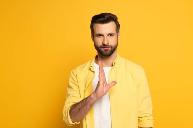 Man showing gesture in deaf and dumb language and looking at camera on yellow background