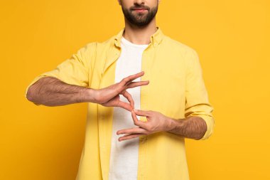 Cropped view of man showing interpretation sign in deaf and dumb language on yellow background