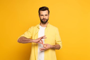 Handsome man showing interpretation sign in deaf and dumb language on yellow background