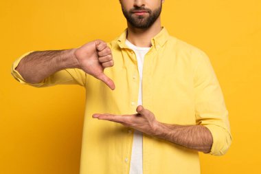 Cropped view of bearded man showing gesture in deaf and dumb language on yellow background