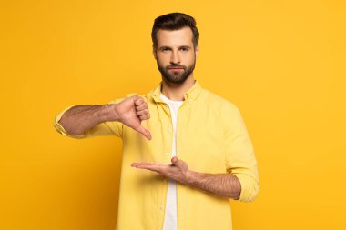 Handsome man showing gesture in deaf and dumb language and looking at camera on yellow background