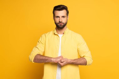 Handsome man showing cohesion sign in deaf and dumb language on yellow background