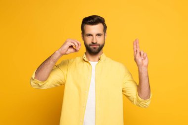 Handsome man showing letters in deaf and dumb language on yellow background