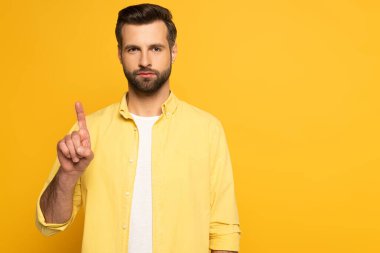 Yakışıklı adam parmağıyla işaret ediyor ve sarı arka plandaki kameraya bakıyor.